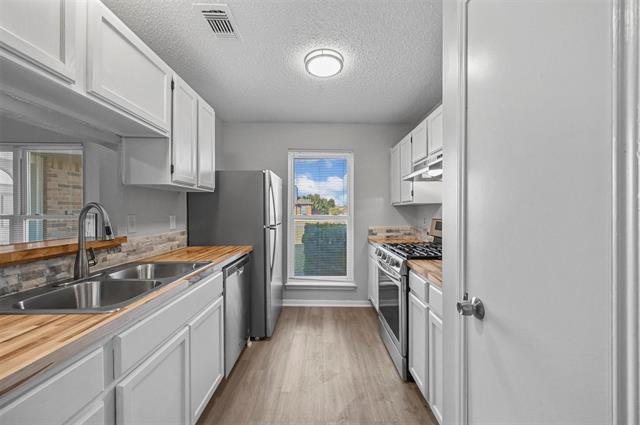 Kitchen with light from updated window, wood-type flooring, dishwasher, a textured ceiling, sink, and white cabinets