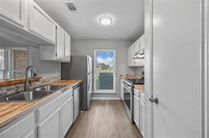 Kitchen with light from updated window, wood-type flooring, dishwasher, a textured ceiling, sink, and white cabinets