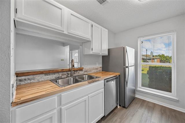 Kitchen with updated window,  white cabinets, gas range, a textured ceiling, light hardwood / wood-style floors, and wood counters