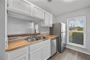 Kitchen with updated window, white cabinets, gas range, a textured ceiling, light hardwood / wood-style floors, and wood counters