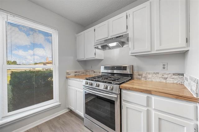 Kitchen with white cabinets, lofted ceiling, stainless steel gas range oven, and wood counters