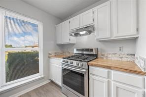Kitchen with white cabinets, lofted ceiling, stainless steel gas range oven, and wood counters