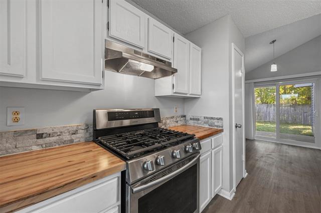 Kitchen with hanging light fixtures, vaulted ceiling, white cabinetry, dark wood-type flooring, and dishwasher