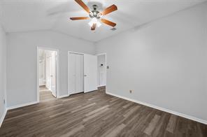Primary bathroom with vanity, toilet, walk-in closet, tiled shower / bath combo, dual sink, wood-look flooring, and vaulted ceiling