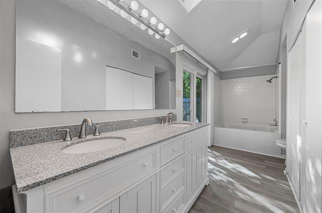Primary bathroom with hardwood / wood-style floors, walk-in closet, a textured ceiling, updated sliding glass door, and tiled shower / bath